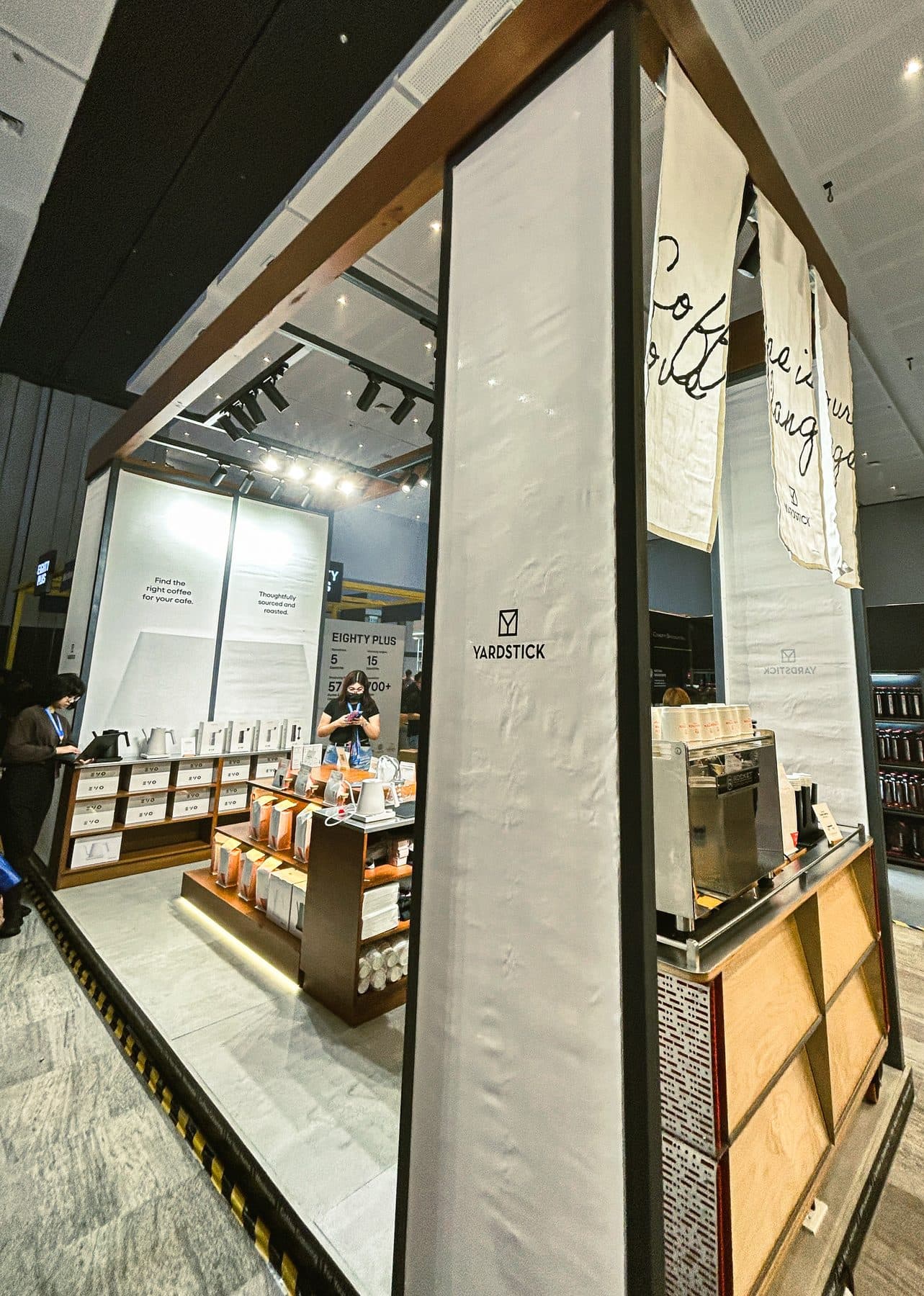 Yardstick booth front with espresso machine, product displays, and hanging banners